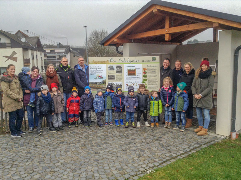Eltern, Kinder und Leitungen der Kita Straßenhaus vor dem neuen Hinweisschild am Schulgarten